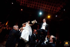 Bride and groom joyfully seated on chairs while guests perform the horah dance during the reception at Capitale in Manhattan, New York.